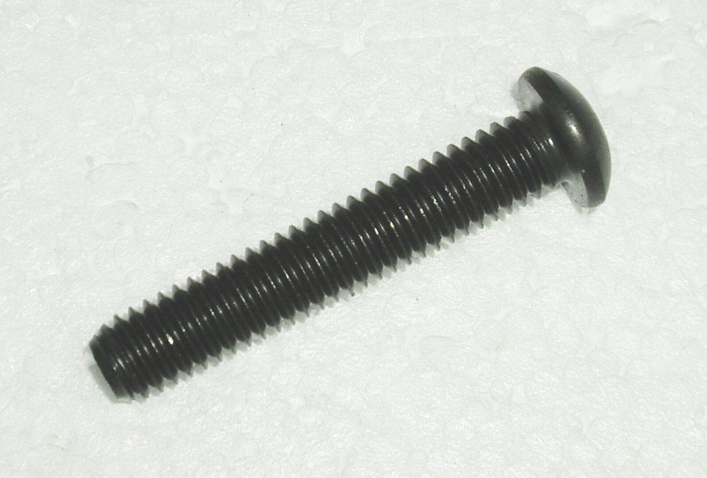 A black screw is sitting on top of the floor.