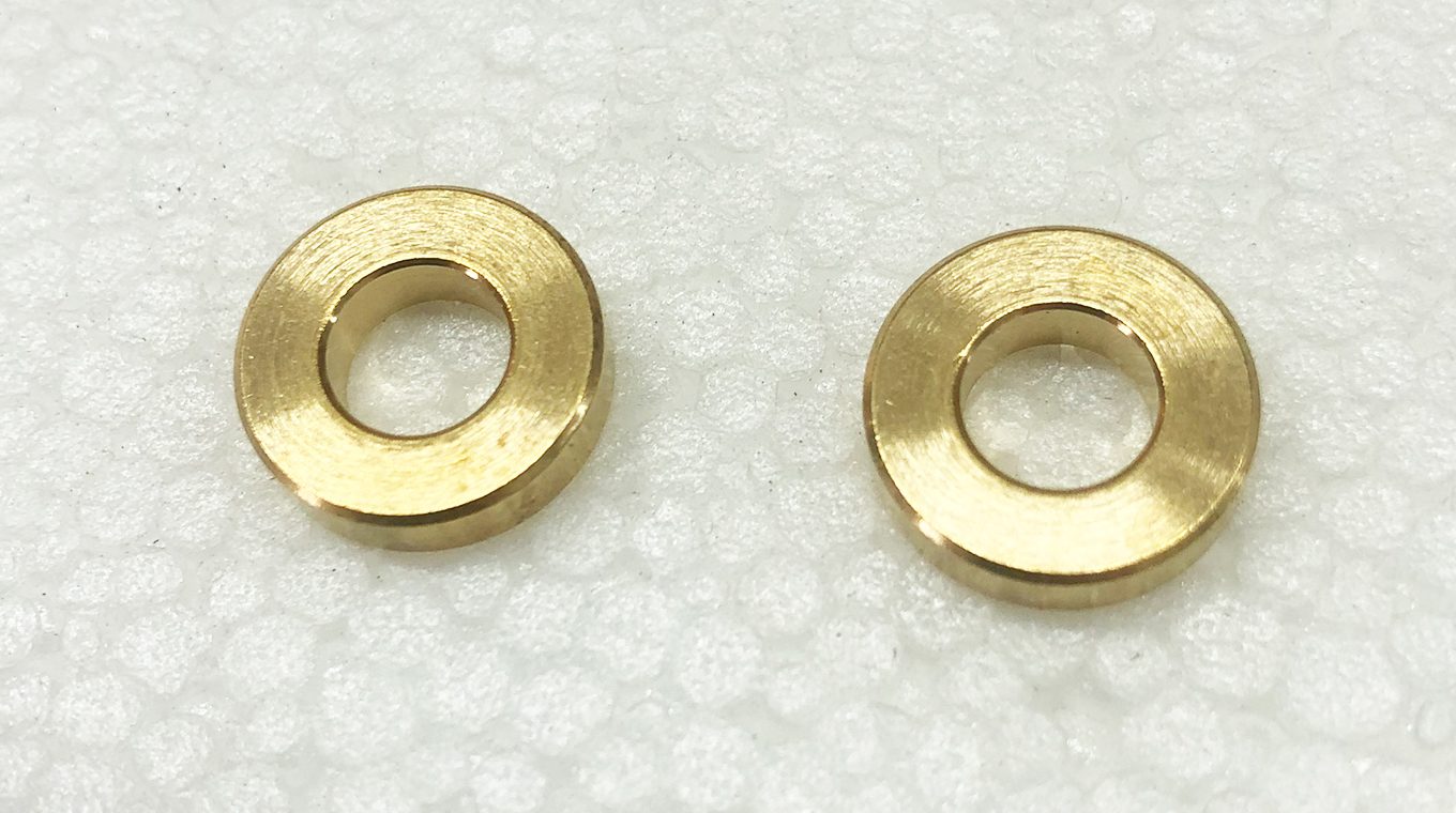A pair of brass washer-like parts sitting on top of a white surface.