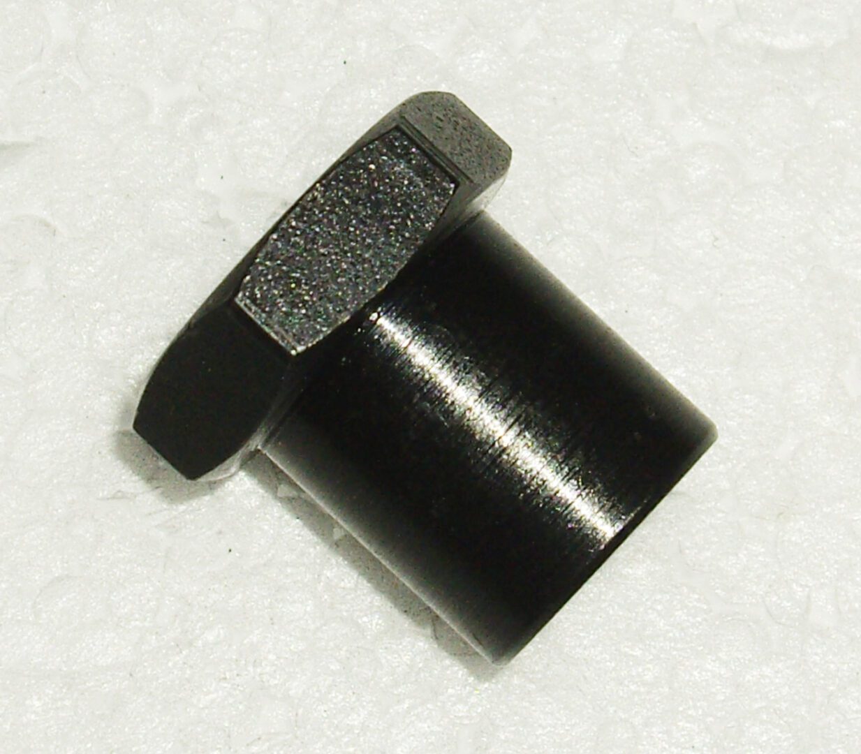 A black plastic nut and washer on the side of a white surface.