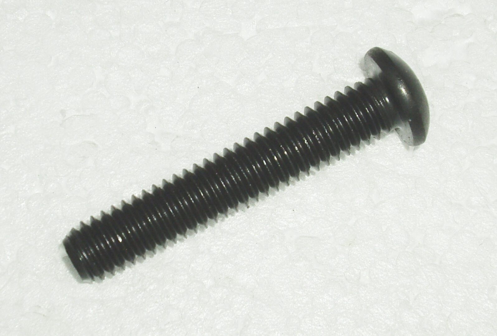 A black screw is sitting on top of the floor.